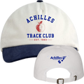 A cream baseball cap with a navy blue ribbed brim, featuring 'ACHILLES TRACK CLUB EST. 1983' and a red apple graphic on the front with a persons silhouette, with a smaller back view showing the adjustable strap and 'Achilles International' logo.
